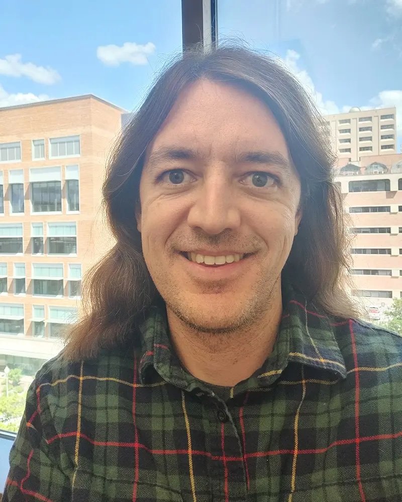 A photo of Joe Stubbs, a middle-aged man with shoulder-length hair and a button-up shirt.